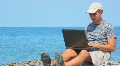 Man With Notebook Sitting On Rocky Beach, Sea In Background