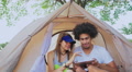 Portrait Of A Smiling Couple Sitting In Tent And Using Tablet In A Forest
