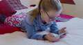 Young Girl Wearing Glasses Lying On Bed Watching A Video On Her Smartphone.