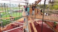 Boy Helping Girl To Get Off Stick Hanging On Ropes In Ropes Park
