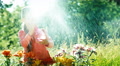 Girl Playing With Sprinkler Near Flowers In The Garden And Smiling