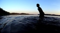 Boy Silhouette Play In Lake, Draw Water Into The Plastic Bag, Summer Evening Sky