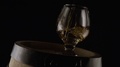 A Glass For Cognac Is On A Wooden Barrel. Black Background. Slow Mo