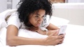 Tired Afro-American Woman Lying In Bed Scrolling And Browsing On Smartphone