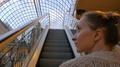 Young Woman Moving On Escalator And Looking Around In Mall