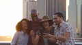 Friends Look At Photos On Phone By Manhattan Skyline At Sunset