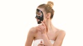 The Happy Woman With A Black Face Care Mask Flirts On The White Background