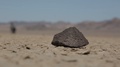 Traveler Walks Behind A Black Volcanic Rock On A Death Valley Desert Ground