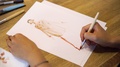 Women's Hands Draw Sketches On Paper With A Brush. A Fashion Designer Or Tailor