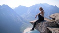 A Beautiful Young Woman Sits On A Mountain Ledge Overlooking A Deep