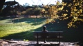 A Woman Sits On A Park Bench In A Park In Porto, Portugal As The Sun