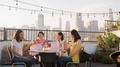 Female Friends Celebrating Birthday On Rooftop Terrace With City Skyline In