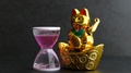 Maneki Neko Japanese Lucky Cat Waving Paw And Hourglass. Time Is Money Concept