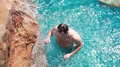 View From The Top As A Man Relaxes In Pool Has Shower Under Waterfall At Sunny