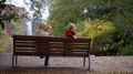 Blonde Woman With Her Little Kids Boy And Girl Are Sitting On Bench In Park Near