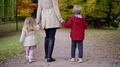 Cute Baby Girl And Boy Are Holding Hands Of Mother Walking In Park In Autumn Day
