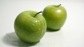 Green Apples On White, Splashed With Drops Of Water. Slow Zoom In.