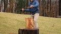 Man Splitting Wooden Log With Axe In Forest