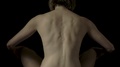 Rear View Of A Nude Woman Sitting Cross Legged And Stretching Her Back