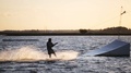Young Wakeboarder Playfully Slides At Speed On River And Jumps From Springboard