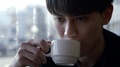 A Close-Up Portrait Of An Asian Brunette Guy Who Drinks A Cappuccino From A Cup