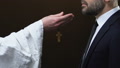 Priest Giving Male Political Wooden Cross Against Black Background, Christianity