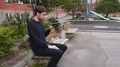 A Man Sitting Alone On A Bench In A Park. Browsing His Smart Phone And