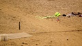 A Neon Green Saturated Kite Flies On A String Along The Beach Where A