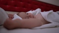 A Small, Naked Baby Sleeps With His Hands Up On A Large Red Bed In Slow Motion
