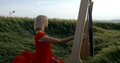 Blonde Woman Is Striking Large Metal Gong In Field Outdoors In Summer Day