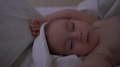 A Small, Naked Child Sleeps With His Hands Up On A Large Bed In Slow Motion