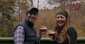 Man And Woman Holding Beer Glasses Sitting Outside On A Deck During The Fall