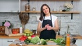 Smiling Beautiful Vegan Female In Apron Posing At Kitchen Surrounded By Fresh