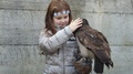 Smiling Little Girl With Crown Of Flowers Caress Tawny Owl On Arm