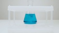 Camera Zooms In On A Glass Flask With Blue Liquid Past A Contain