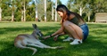 Young Malaysian Woman Feeding A Red Kangaroo Laying In The Grass