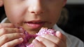 The Child Slowly Bites Into A Delicious Doughnut With Pink Icing. Mouth Close-Up