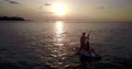 Slow Motion View Of Two People In A Paddle Board At Sunset. Silhouette Of Two C