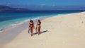 Two Girls Holding Flippers While Walking Along The Shore, Leaving Footprints On
