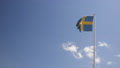 Swedish Flag Waving In The Wind Against A Blue Sky. Slow Motion Footage.