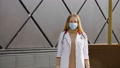 Happy Female Doctor Or Nurse In Surgical Mask And White Medical Gown Walks