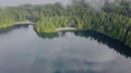 Fly Over The Lake With The Forest On Background And Low Clouds In The Morning
