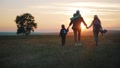 Silhouettes Of Mother With Two Kids Hiking On Nature On Sunset. Concept Of