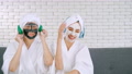 Two Happy Asian Girls In White Bathrobes With Facial Mask Enjoying Music
