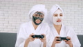 Two Happy Asian Girls In White Bathrobes With Facial Mask Playing Video Game