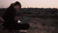 Camera Rotates Around Modern Styled Girl Working On Laptop In A Field In Sunset