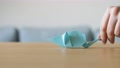 A Hand Moving A Cute Stylized Blue Handmade Origami Mouse On A Wooden Table.