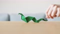 A Hand Moving A Cute Stylized Green Handmade Origami Snake On A Wooden Table.