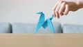 A Hand Moving A Cute Stylized Blue Handmade Origami Horse On A Wooden Table.