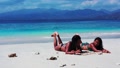 Two Girls Sunbathing On The Beach As They Lie Flat On The Sand And Play A Game